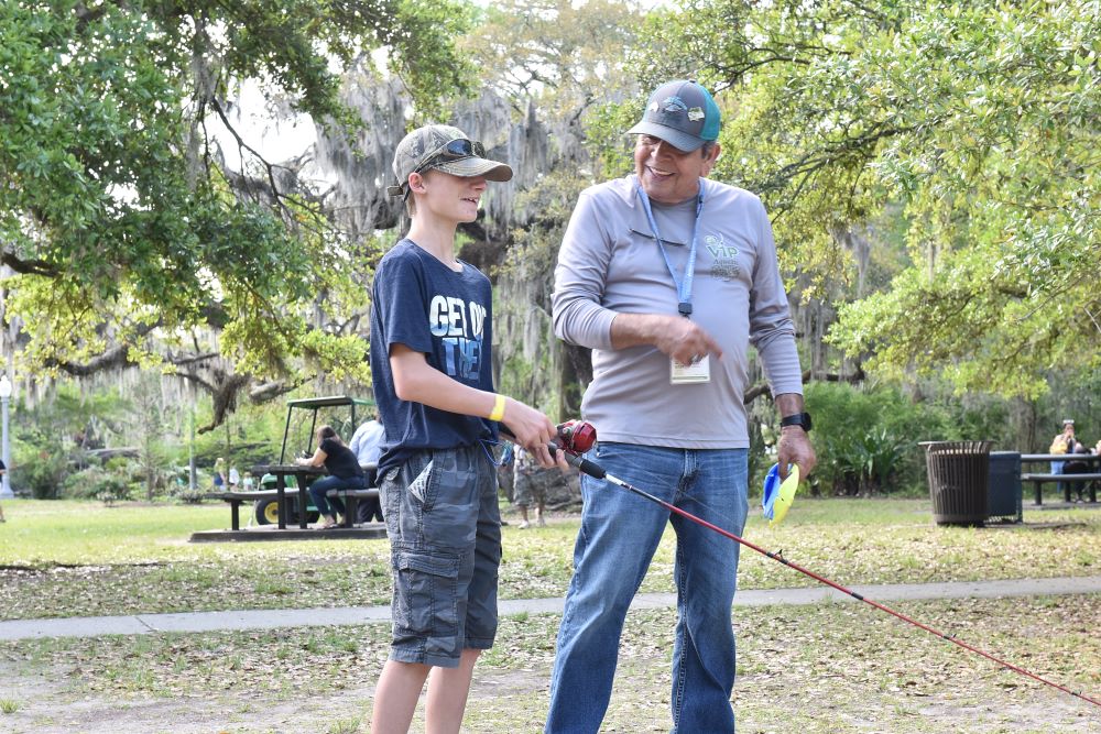 quatic Volunteer Instructor, Ed Richards, assist a youth participant with casting instruction.